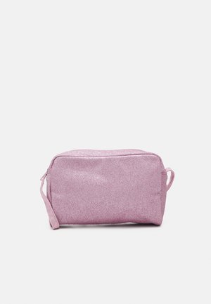 Trousse de maquillage rectangulaire rose pailletée avec fermeture éclair et petite anse en boucle sur un côté, sur fond uni.