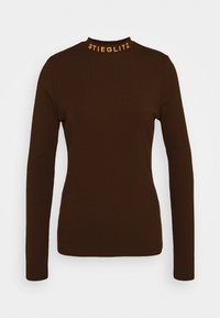 Brązowa bluzka z długim rękawem oraz wysokim kołnierzem, z pomarańczowym napisem "STIEGLITZ" na kołnierzu. Gładka, dopasowana tkanina z minimalnymi zdobieniami.
