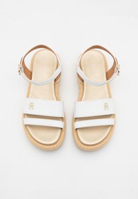 White leather sandals with two wide straps, metallic gold footbed, and woven espadrille-style sole. Adjustable ankle strap with buckle detail.