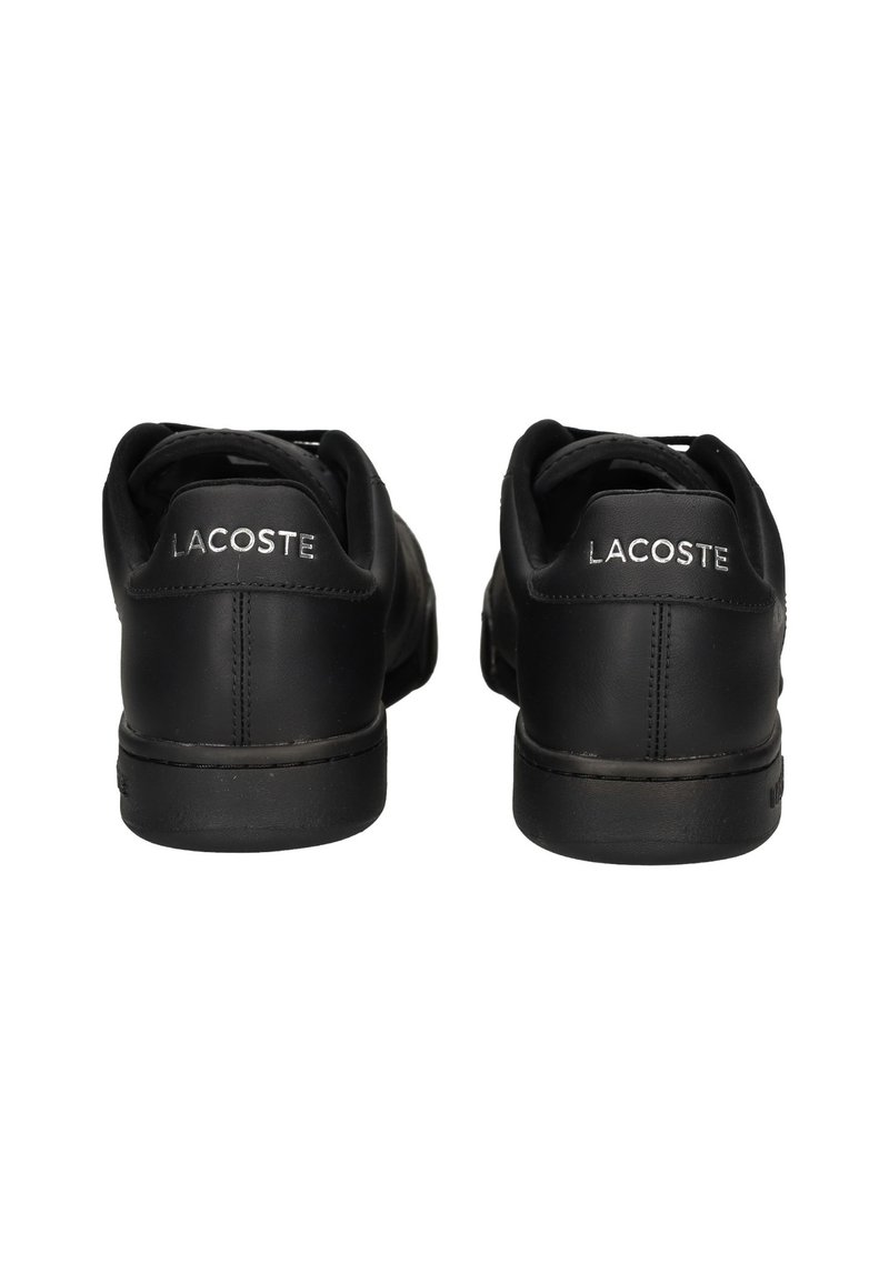 Baskets en cuir noir avec bouts arrondis, design profilé et logo métallique "LACOSTE" sur le talon arrière. Semelles plates en caoutchouc noir.