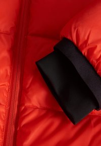 Rode pufferjas met een ritsluiting, voorzien van elastische zwarte manchetten en een gewatteerde textuur. Glad, lichtgewicht stof met zichtbare stiksels.