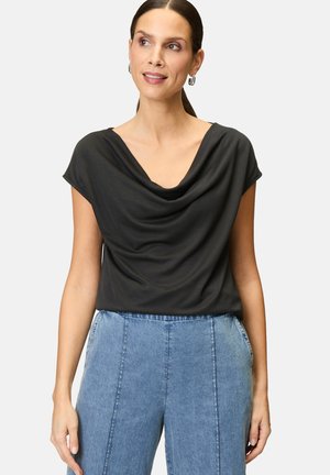 Schwarzes drapiertes Oberteil mit kurzen Ärmeln und weitem Ausschnitt. Kombiniert mit hellblauen, hoch taillierten Jeans. Glatte Textur.