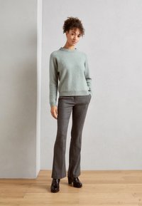 Un pull en laine vert clair, un pantalon gris évasé et des chaussures à talons noires. La tenue présente une coupe décontractée et des textures subtiles.
