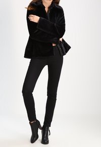 Czarna kurtka z sztucznego futra o lekko rozszerzonym kroju, z wysokim kołnierzem i szerokimi mankietami, zestawiona z czarnymi dopasowanymi spodniami i botkami za kostkę.