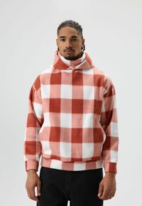 Pullover hoodie met een groot rood-wit geruit patroon, gemaakt van zachte, gestructureerde stof. Voorzien van een hoge kraag en een losse pasvorm.