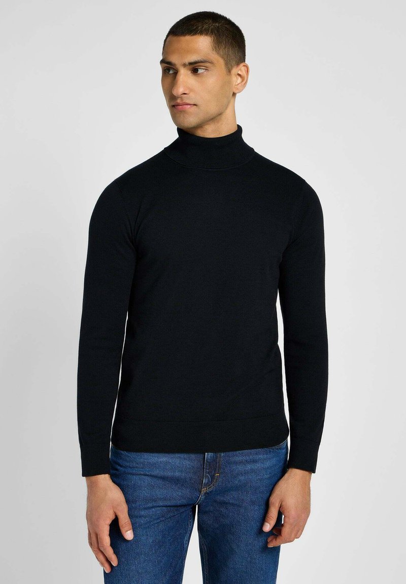 Maglione a collo alto nero con maniche lunghe, realizzato in un tessuto dalla texture liscia, abbinato a jeans in denim blu. Design minimalista, senza motivi o accenti.