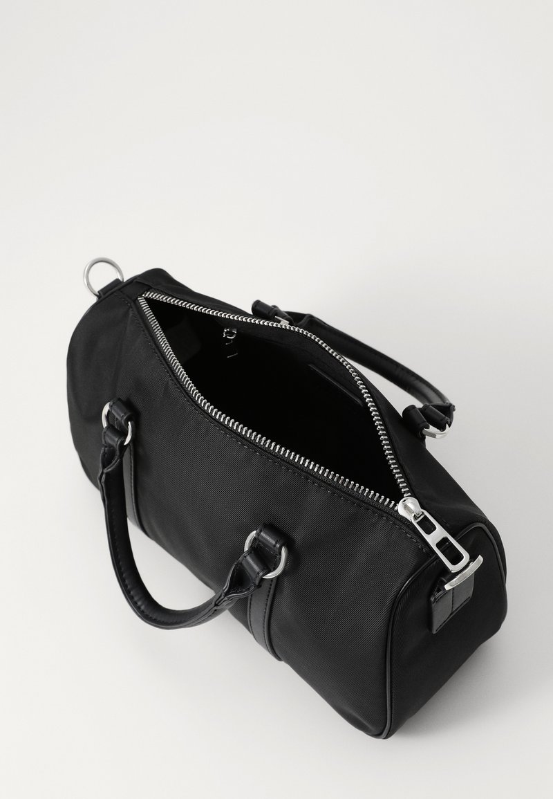 Borsone in tessuto nero con zip argentata, apertura superiore, doppie maniglie e clip laterale per attacco. Texture liscia e forma strutturata.