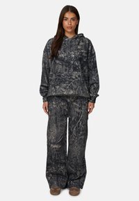 Komplet dresowy z kapturem w ciemnoszarym kolorze w kamuflażu, wykonany z teksturowanej tkaniny. Charakteryzuje się luźnym krojem i podszytym kapturem dla dodatkowego ciepła.