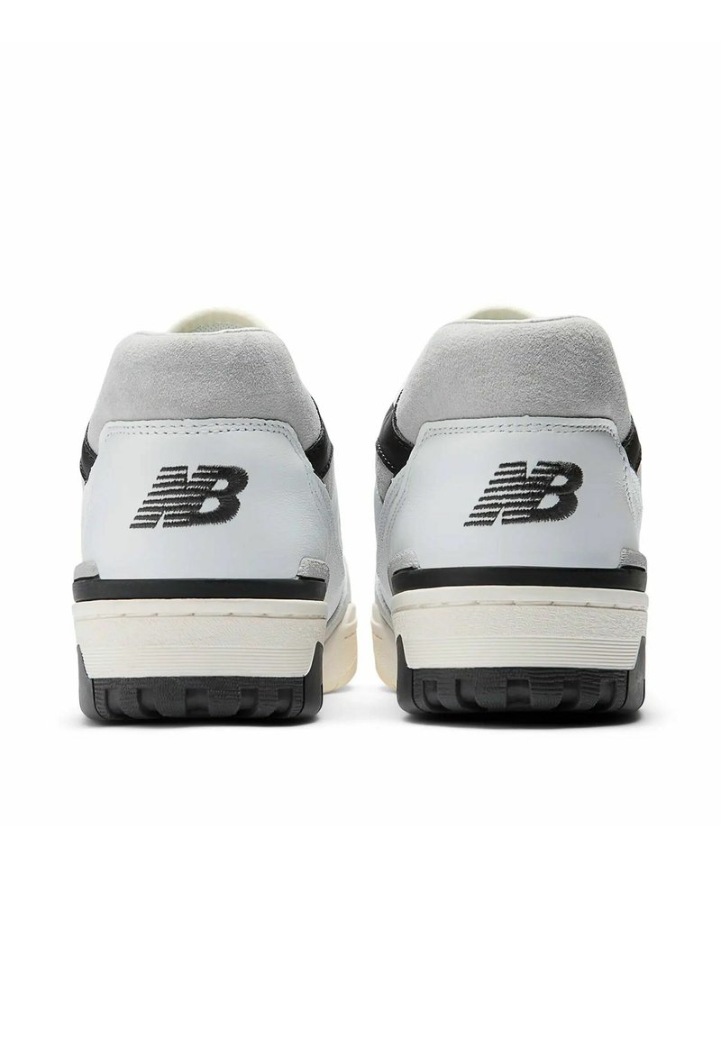 Baskets en cuir blanc avec des accents en suède gris, des détails noirs, des semelles en caoutchouc plates et un dos texturé arborant le logo New Balance.