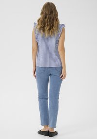 Haut sans manches rayé bleu et blanc avec des volants sur les épaules, associé à un jean bleu clair et des ballerines noires.