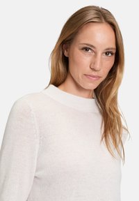 Lekki, kremowy sweter z wysokim dekoltem, długimi rękawami i miękkim, teksturowanym materiałem. Posiada luźny krój i minimalistyczny design.