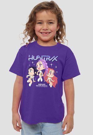 Lila Baumwoll-T-Shirt mit einem Grafikdruck von drei Comicfiguren in lebhaften Farben, die in K-Pop-Outfits gestylt sind, und großem "HUNTRX"-Text.