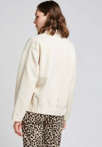 Veste en polaire crème avec une coupe décontractée, ourlet côtelé et épaule tombante, associée à un pantalon imprimé animal.