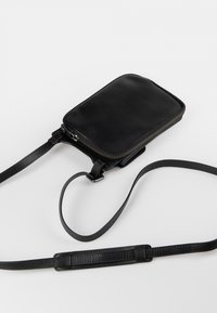Borsa a tracolla in vera pelle nera con forma rettangolare, chiusura a zip e tracolla rimovibile. Presenta una texture liscia e un design minimalista.