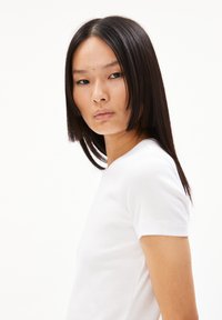 Hvid ribbet t-shirt med korte ærmer, der har en rund halsudskæring og en tætsiddende silhuet, båret af en model med langt, glat hår.