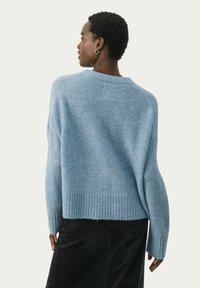 Pull léger bleu en matériau doux avec un ourlet large et côtelé et une texture subtile. Il présente une coupe décontractée et des épaules tombantes.