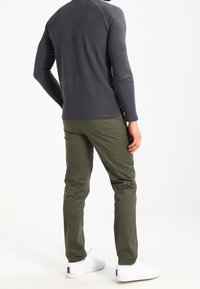 Maglietta grigia a maniche lunghe con finitura testurizzata, abbinata a pantaloni aderenti verde oliva e sneakers bianche, vista da dietro.