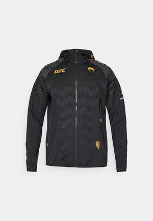 Crna jakna na patentni zatvarač s kapuljačom, žutim detaljima, teksturiranim dijamantnim uzorkom i UFC logotipom na prsima i rukavu.