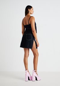 Átlátszó crop top állítható pántokkal, magas derekú farmer szoknyával, amely oldalsó hasítékokkal rendelkezik. Rózsaszín platform sarkú cipővel viselve.