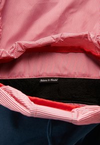 Tissu rayé rouge et blanc doublant un sac ouvert avec une étiquette intérieure noire où est inscrit "Welcome to Herschel."