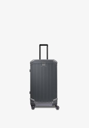 Maleta rígida hecha de material duradero gris oscuro. Cuenta con textura acanalada, asa telescópica y cuatro ruedas giratorias para mayor movilidad.