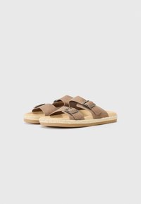 Sandales en suède marron avec deux larges sangles et des accents de boucles. Semelle tissée naturelle avec une finition texturée. Semelle intérieure rembourrée douce.