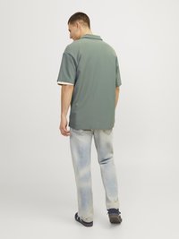 Grøn kortærmet polo shirt med en afslappet pasform og lyse accenter, parret med bleget blå ripped jeans og mørke sko.