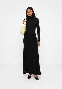Črna dolga obleka z dolgimi rokavi in turtleneck obliko, elegantne silhuete in ohlapnim krojem. V kombinaciji s svetlo rumeno torbico in črnimi čevlji s koničastim prstom.