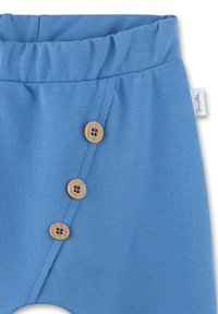 Blaue Stoffhosen mit einem elastischen Bund, ausgestattet mit vier Holzknöpfen an der Seite und einem kleinen Markenlabel an der Naht.