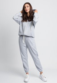 Szara bawełniana bluza z kapturem na zamek, z troczkami i luźnym krojem, w połączeniu z dopasowanymi dresami; noszona z białymi trampkami.