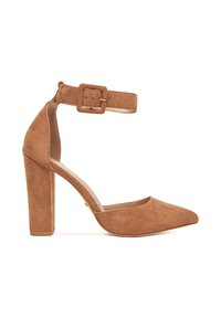 Zapato de tacón alto de ante marrón con punta afilada y correa en el tobillo con hebilla rectangular. Superficie texturizada y diseño de tacón cuadrado.