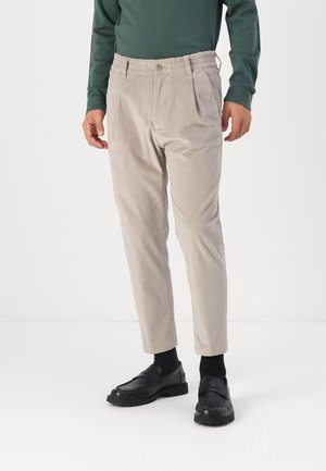 Beige cordbukser med elastisk talje og knap, brugt med sorte sokker, sorte loafers og en mørkegrøn langærmet top.