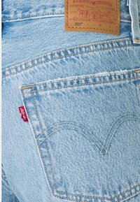 Ljusblå denimjeans med en läderetikett; har en röd Levi's-flik och gul söm. Anmärkningsvärd design på bakfickan med böjd söm.