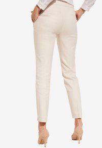 Beige taillierte Hose aus glattem Stoff, mit schlanker Passform, zwei Gesäßtaschen und einer verkürzten Länge. Schlichtes Design ohne Muster.