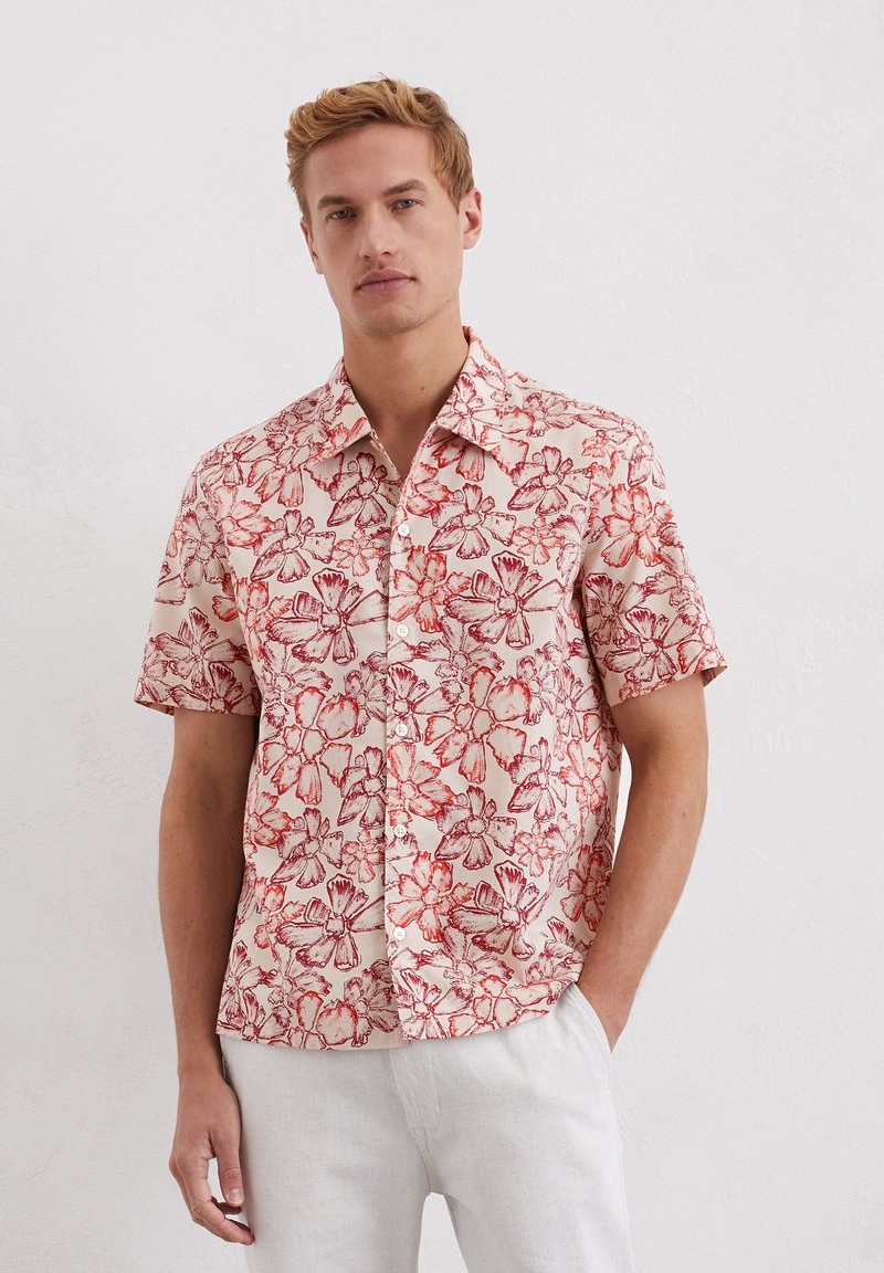 Korte mouwen shirt van lichtgewicht stof met een bloemmotief in rood op een lichtbeige achtergrond; knoopsluiting aan de voorkant en kraag.