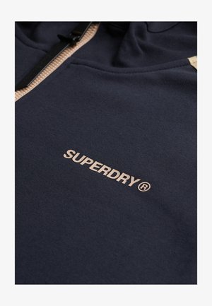 Marineblaues Sweatshirt aus strukturiertem Stoff, mit einem sichtbaren Reißverschluss und einem hellbraunen, auf der Vorderseite gestickten Logo.