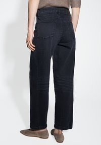 Pantalons en denim foncé avec une coupe décontractée, cinq poches et des détails de couture visibles. Le tissu semble lisse avec un léger éclat.