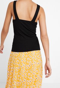 Top negro de canalé con tirantes anchos, combinado con una falda amarilla con flores que presenta flores blancas y rosas. Material texturizado con frunces.