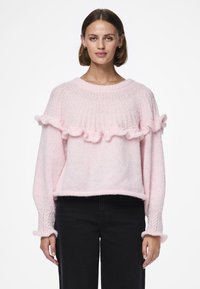 Pull en tricot rose avec une texture côtelée, doté d'un ourlet et de poignets volantés. La coupe ample s'harmonise avec un style décontracté.