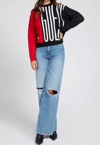 Pull rouge et noir avec de grandes lettres blanches audacieuses, associé à un jean large déchiré bleu clair et des bottines noires à talons.