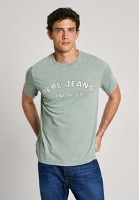 Šviesiai žalias medvilninis marškinėlis su užrašu "PEPE JEANS LONDON W11", atspausdintu baltai, su apvaliu kaklu, trumpomis rankovėmis ir laisvu siluetu.