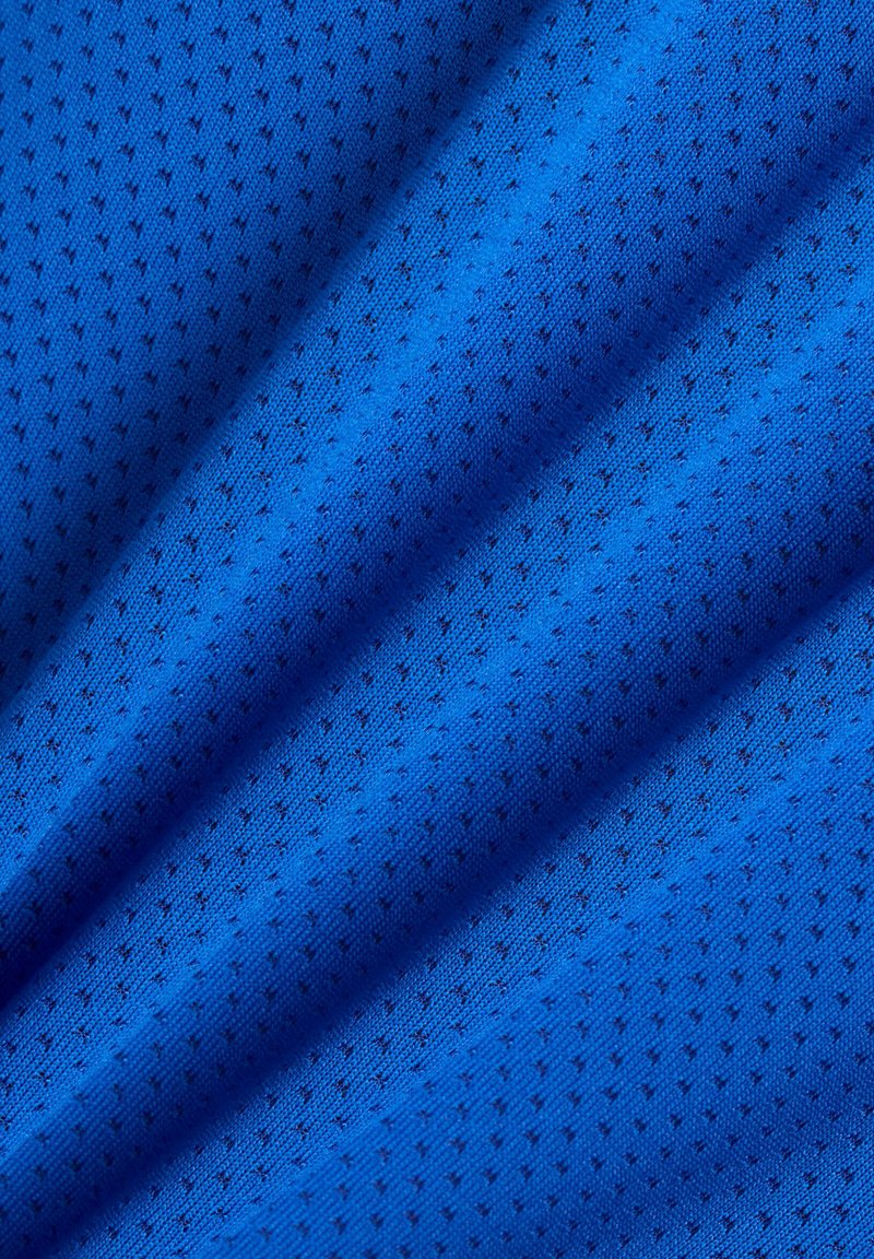 Getextureerde blauwe stof met een lichte, gaasachtige uitstraling, met een herhalend patroon van kleine, donkere stippen over het geheel.