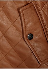 Pelle marrone trapuntata con un motivo cucito prominente, un piccolo bottone logo in metallo nero e un dettaglio con tasca a toppa.