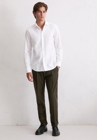 Witte, geknoopte blouse, gecombineerd met donkergroene broek. Model draagt zwarte schoenen. Eenvoudig, klassiek ontwerp met een gladde textuur.