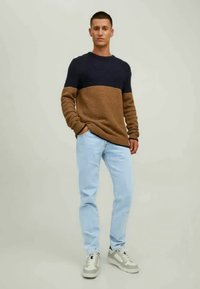 Pull en maille bleu foncé et beige, avec un design texturé, associé à un jean bleu clair et des baskets grises.