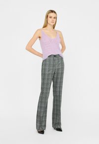 Lilac strikket tanktop med åbent vævdetalje, parret med højtsiddende, grå ternede bukser og sorte spidse hæle.