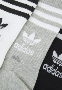 Trois paires de chaussettes en blanc, gris et noir ; texture côtelée avec des rayures horizontales et un logo blanc représentant trois feuilles.