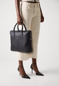 Black leather tote bag with top handles, zip closure, front pocket, and silver hardware. Smooth texture, structured design.