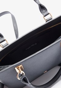 Sac à main en cuir noir avec ferrures dorées, fermeture éclair supérieure ouverte et étiquette "ANNA FIELD" visible à l'intérieur.