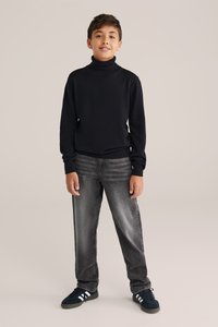 Melnas turtlenecks džemperis, šaura piegriezuma, ribotas aproces un apakšmalas, kopā ar gaiši pelēkiem džinsiem. Tenisēm ir tumši zilas pamats un baltas svītras.